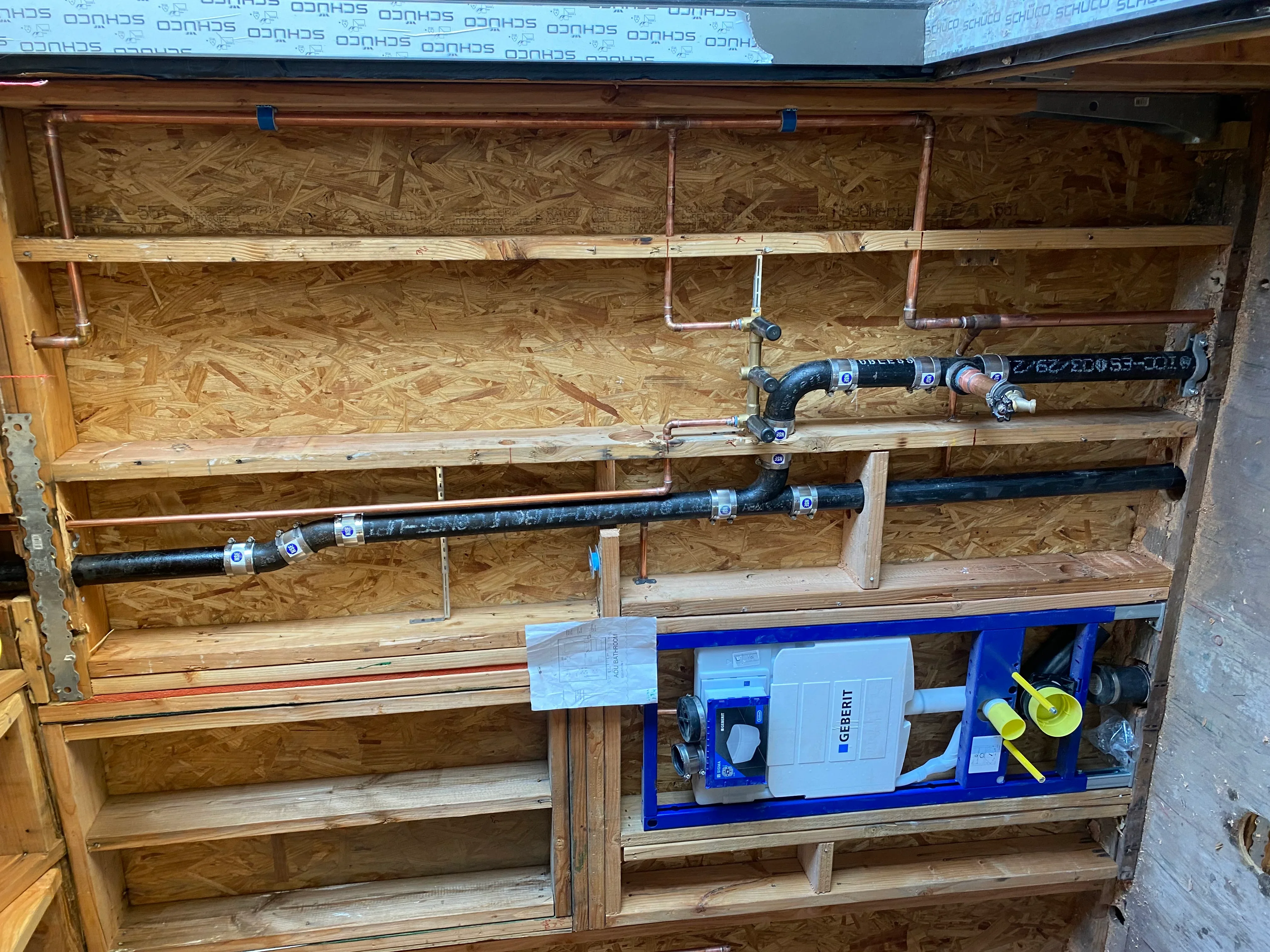 Copper and PVC plumbing lines with straps, wooden framing, and tankless water heater unit installation