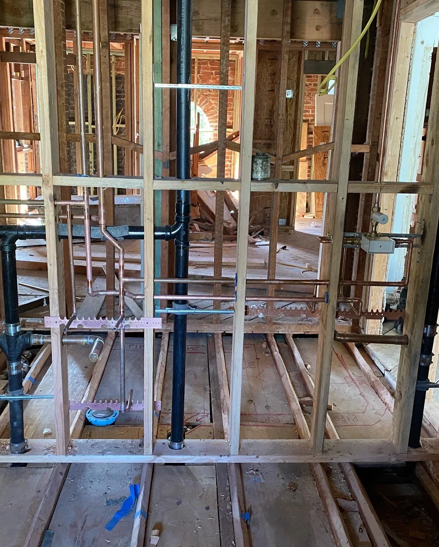 Black PVC drain lines and copper piping rough-in installation within wood-framed walls during construction