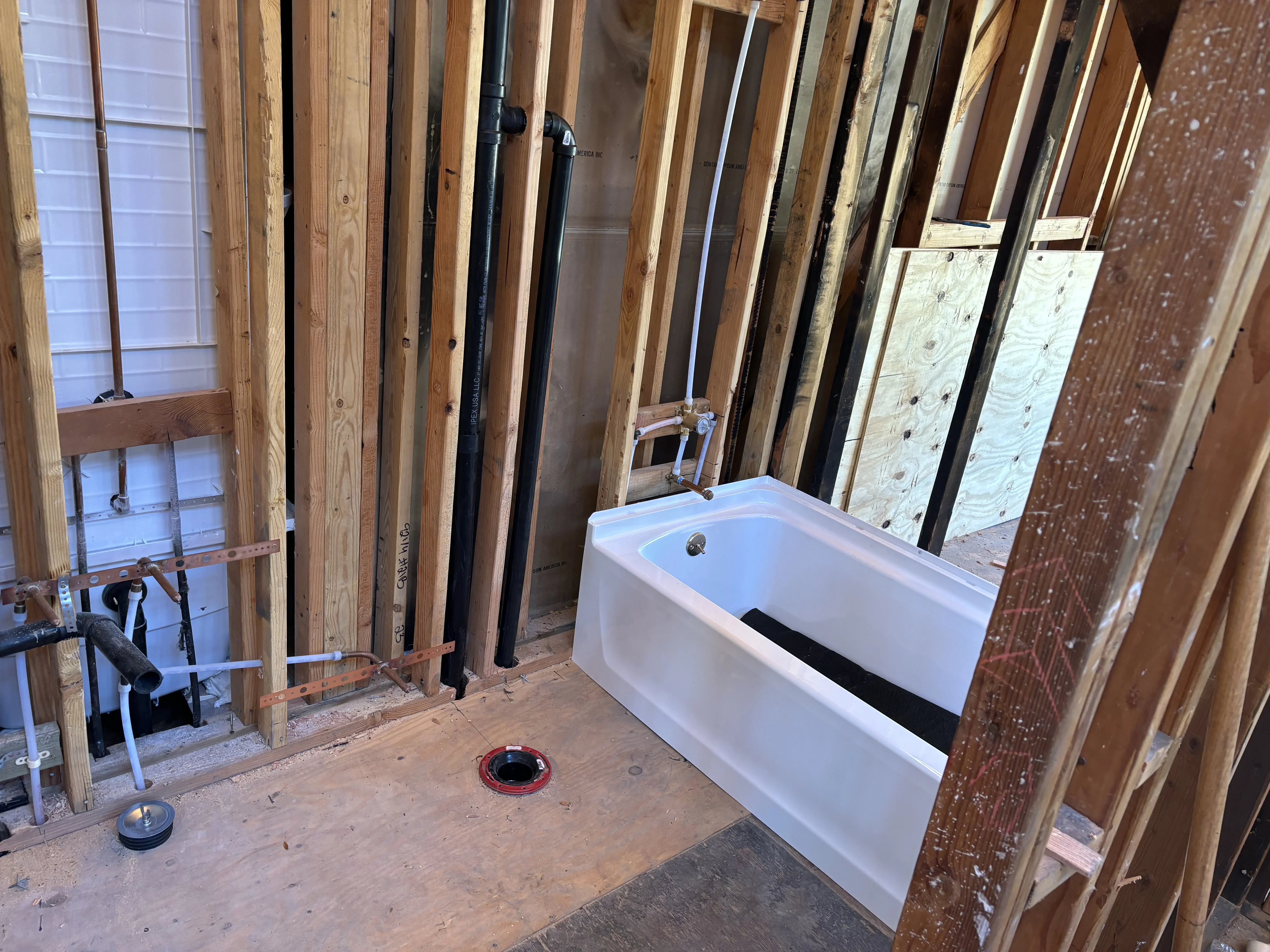Bathroom rough-in with white soaking tub, black vent stack, and copper supply lines in framed walls