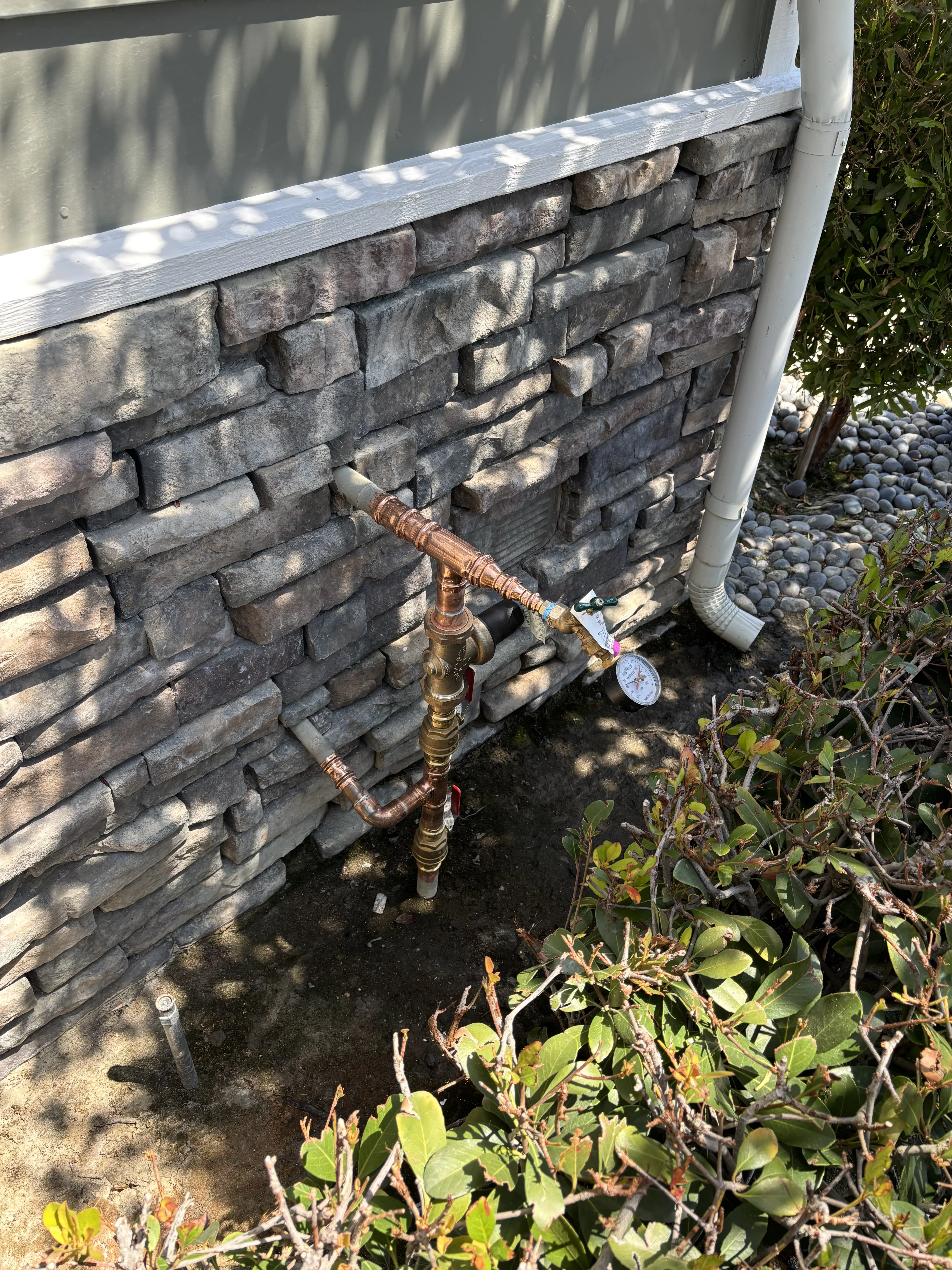 Brass outdoor spigot with copper piping installed on stone veneer wall with shut-off valve and pressure gauge